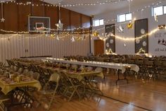 tables and chairs are set up in the middle of a room with lights strung from the ceiling