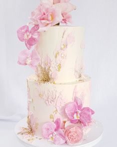 a three tiered cake with pink flowers on the side and gold leaf decoration around the edges