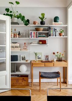 a desk and shelves in a room with plants on top of the bookshelves