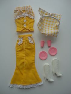 doll clothes and accessories are laid out on a white surface, including a yellow dress