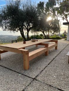 a wooden table sitting on top of a cement ground next to some trees and bushes