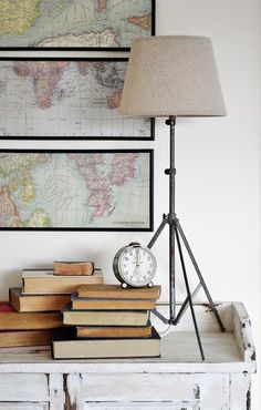 a lamp on top of a table next to some books and a clock in front of a map