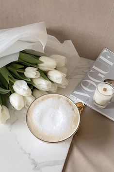 white tulips and a cup of coffee sit on a marble table next to a book