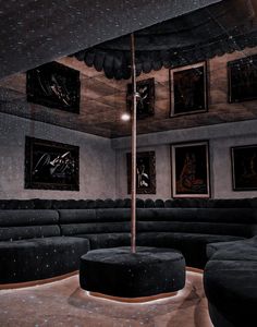 a room with black couches and pictures on the wall above them, along with round ottomans