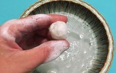 a hand is holding two balls of soap in a bowl with water on the side