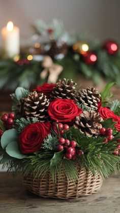 a basket filled with red roses and pine cones on top of a table next to candles