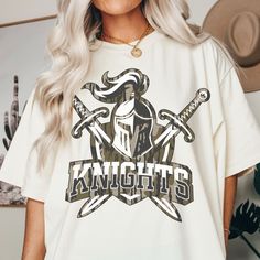 a woman wearing a white knights t - shirt with two crossed swords on the front