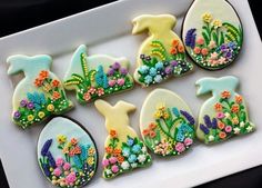 some decorated cookies in the shape of animals on a white tray with flowers and plants