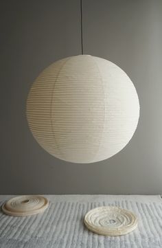 a white lamp hanging from the ceiling over a bed with two rolls of fabric on it