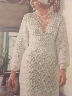 an old photo of a woman wearing a white dress and pearls on her head, standing in front of a mirror