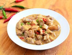 a white bowl filled with meat and vegetables on top of a wooden table next to red peppers