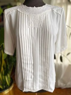 "Vintage 90s white blouse with a floral collar by Nicola. Pleated in the front and buttons at the back of the neck. 100% polyester. Condition: Great. No holes. Has two super faint stains. See photos. Size: tagged 10. Best fit M. Always refer to measurements for more accurate sizing. Measurements taken laying flat: STS: 16\" PTP: 19\" L: 25\" ALL SALES ARE FINAL SO PLEASE DOUBLE CHECK THE MEASUREMENTS PRIOR TO BUYING AND DON'T HESITATE TO REACH OUT IF YOU HAVE ANY QUESTIONS!  All items are vintage/preloved and may have small imperfections. This should be expected for secondhand clothing. ALL MAJOR FLAWS WILL BE NOTED IN THE DESCRIPTION AND PHOTOGRAPHED." Classic Lace Top For Workwear, Classic Lace Top For Work, Classic Summer Tops With Lace Trim, Classic Summer Shirt With Lace Trim, Elegant Summer Tops With Peter Pan Collar, Vintage White Summer Blouse For Daywear, White Blouse With Peter Pan Collar For Spring, Elegant Peter Pan Collar Top For Summer, White Lace Collar Top For Spring