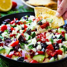 a person dipping a tortilla into a black bowl filled with vegetables and cheese