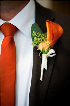 a boutonniere with an orange flower and greenery on the lapel