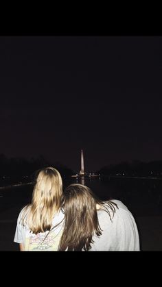 two people are standing in front of the washington monument at night with their backs to each other