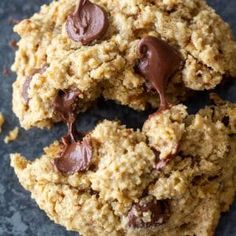 two cookies with chocolate chips are on a black surface and one cookie has been cut in half