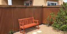 a wooden bench sitting in front of a fenced in area next to a house