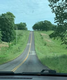 the view from inside a car looking at a road with trees and grass on both sides