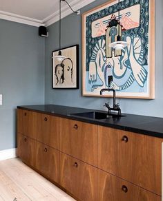 a kitchen with blue walls and wooden cabinets in the center is an art work on the wall