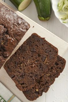 two slices of chocolate zucchini bread on a cutting board next to cucumbers