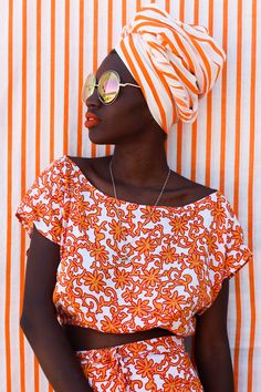 a woman in an orange and white top with sunglasses on her head is leaning against a striped wall