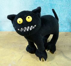 a black stuffed animal with big yellow eyes and fangs on it's back legs