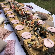 a long table is set with pink plates and place settings for an outdoor dinner party