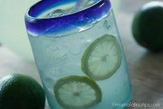 a glass filled with ice and limes on top of a table next to two limes