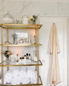 a bathroom with gold shelving and shelves filled with white towels, candles and flowers