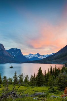 the sun is setting over a lake with mountains in the background and trees around it