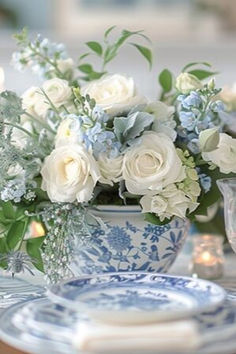 a blue and white floral centerpiece on a table with plates, candles and napkins