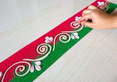 someone is painting the side of a red and green christmas ribbon with white flowers on it