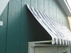 a green building with a striped awning over the door and window sill on the side