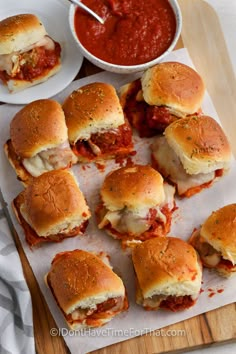 several mini sandwiches on a cutting board with sauce