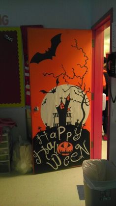 an orange door decorated with a happy halloween scene and bats on the top, next to a trash can