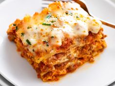 a white plate topped with lasagna covered in sauce and cheese next to a fork