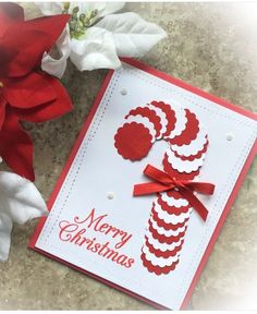 a red and white christmas card with a candy cane on it next to some flowers