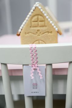 a gingerbread house shaped cookie sitting on top of a white chair with pink ribbon