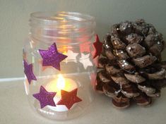 a pine cone sitting next to a glass jar filled with glitter stars and a lit candle