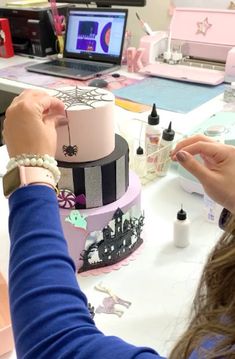 a woman is decorating a pink and black cake