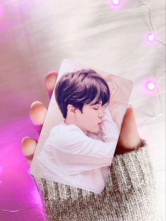 a hand holding a card with an image of a boy on it in front of pink lights