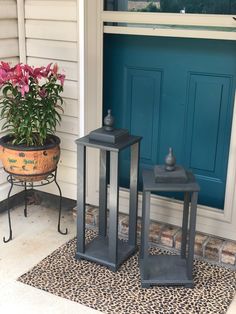 two metal lanterns sitting on top of a rug next to a potted plant in front of a blue door