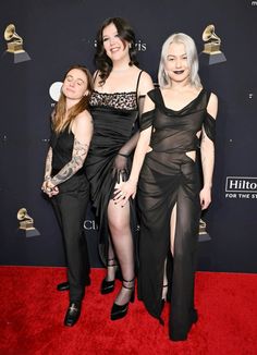 three women in black dresses posing on the red carpet at an awards event with one woman wearing