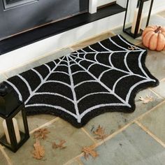 a black and white spider web rug on the ground next to a lantern, pumpkins and lanterns