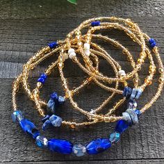 blue and gold beaded bracelets sitting on top of a wooden table next to a plant