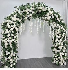 white flowers and greenery are arranged in an arch