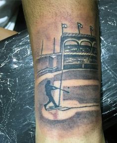 a man with a baseball bat on his arm and a tattoo that has a boat in the background