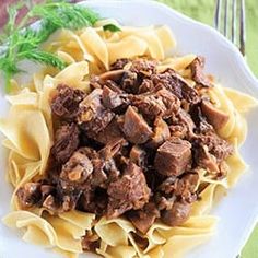 a white plate topped with pasta covered in meat and sauce on top of a wooden table