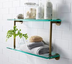 two glass shelves with towels, soaps and other items on them against a white tiled wall