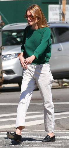 a woman walking across a street wearing white pants